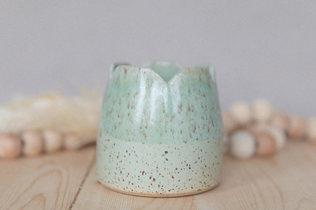 Speckled green ceramic cup on a wooden surface with a neutral background